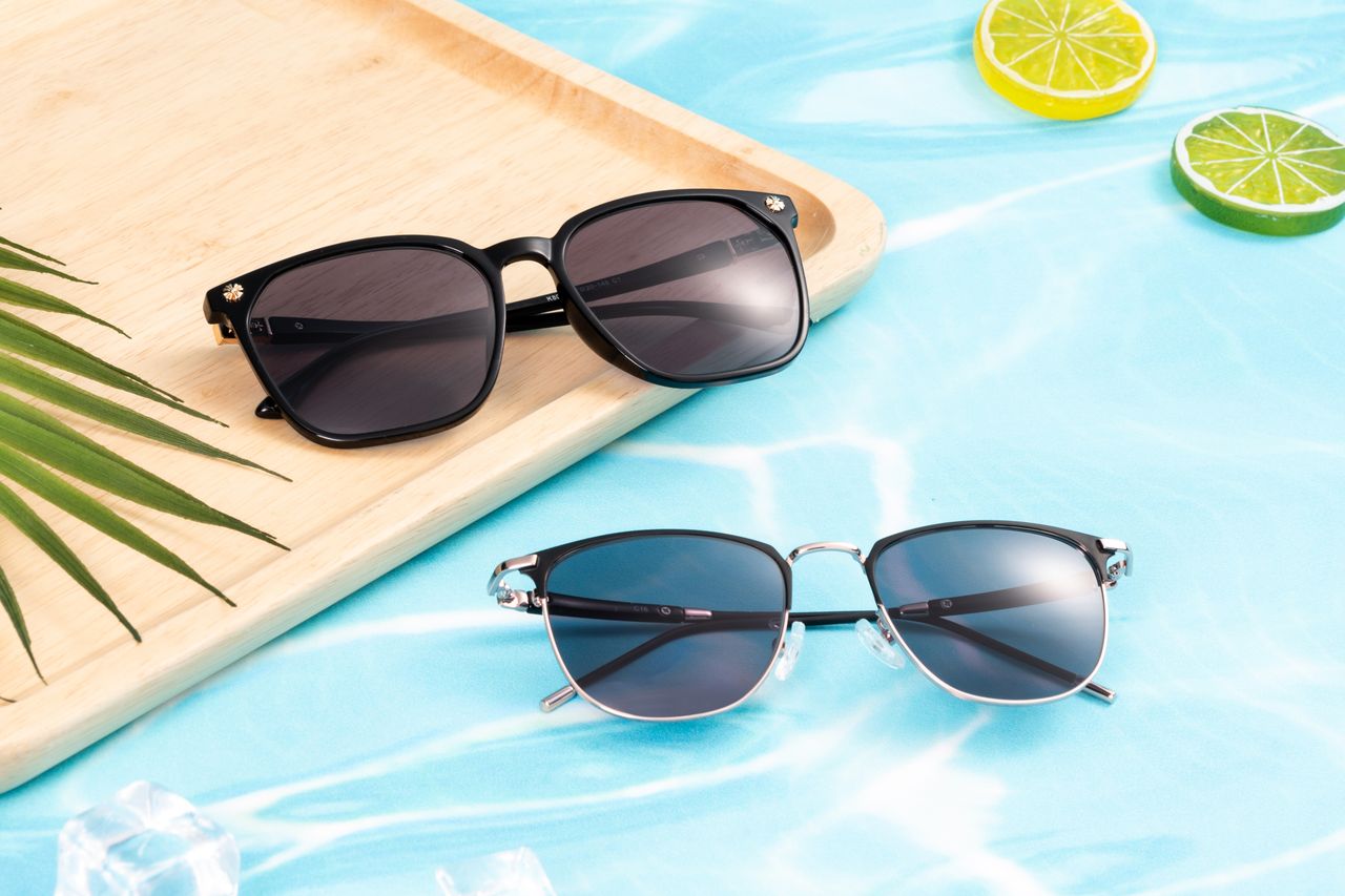 Elegant sunglasses on a wooden tray by a pool, evoking summer vibes with lime slices and palm leaf.